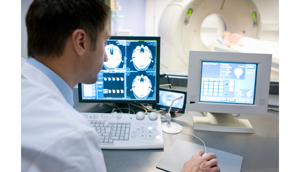 Clinician reviewing imaging beside a CT scanner.